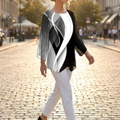 Woman walking a city street at golden hour in a geometric print tunic top, white trousers and loafers